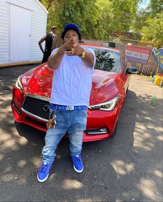 a man standing in front of a red car pointing at the camera with his finger