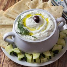 a plate with crackers, cucumber and pita chips on it next to a bowl of dip