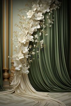 a tall white flower arrangement in front of a green drapeed curtain with gold vases