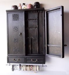 an old black cabinet is hanging on the wall next to some bracelets and rings