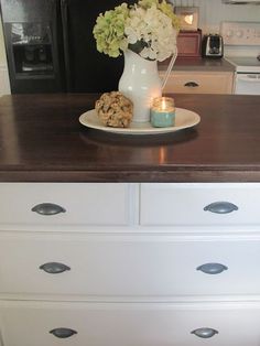 a white vase with flowers on top of a dresser