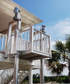 a white house with two balconies next to the water and palm trees in front of it