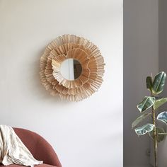 a round mirror hanging on the wall next to a chair with a plant in it