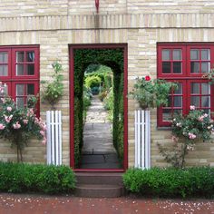 an open door leading to a brick building with red shutters and flowers on either side