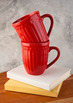 two red coffee mugs sitting on top of each other next to a stack of books