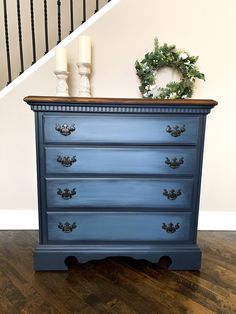 a blue dresser with candles and wreath on top in front of a stair case next to a banister