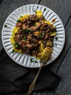 a white plate topped with pasta covered in meat and sauce on top of a wooden table