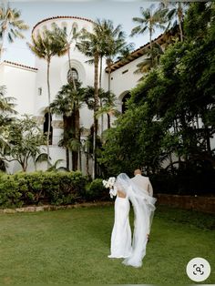 a bride and groom walking in front of a large white building with palm trees around them