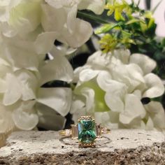 an emerald colored ring sitting on top of a rock next to white hydrangeas