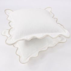 two white scalloped pillows sitting on top of each other in front of a white background