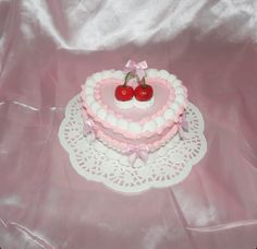 a heart shaped cake with two cherries on top, sitting on a doily