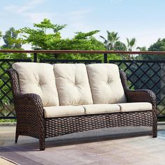 a wicker couch sitting on top of a patio next to a swimming pool with trees in the background