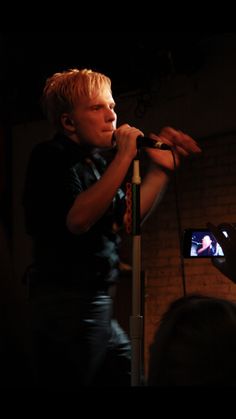 a man standing in front of a microphone on top of a tripod next to a brick wall