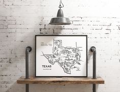 a framed texas map on a wooden shelf in front of a white brick wall with an industrial light