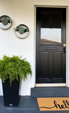 a black front door with two potted plants on the side and a welcome mat that says hello