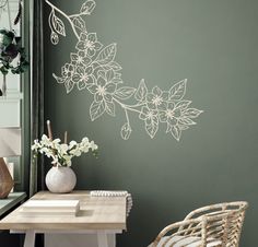 a white vase with flowers on a table next to a green wall