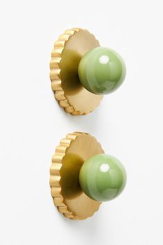 two green knobs on the side of a white wall and one has a gold finish