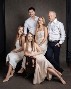 a group of people posing for a photo in front of a gray background with one woman sitting on a chair