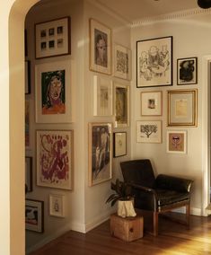 a living room filled with lots of framed pictures on the wall above a leather chair