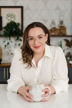 a woman sitting at a table with a coffee mug in front of her and smiling