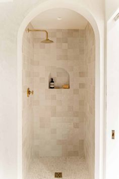 a white tiled shower with gold faucet and soap dispenser on the wall