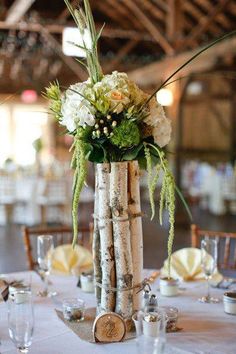 a tall vase filled with flowers and greenery on top of a white table cloth