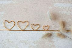 three heart shaped gold wire hangers on a white background with dried grass in the foreground