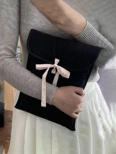 a woman wearing a gray sweater holding a black and white purse with a pink ribbon on it