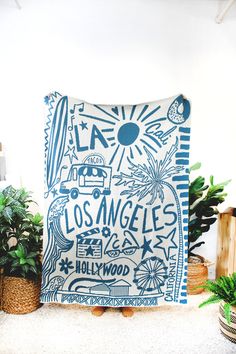 a blue and white pillow with the words los angeles printed on it next to potted plants