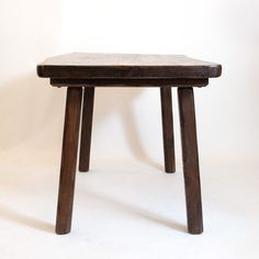 a small wooden table with two legs and a white wall in the backround