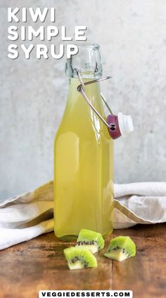 a bottle filled with liquid sitting on top of a wooden table next to sliced kiwi