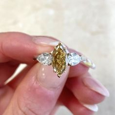 a woman's hand holding a fancy ring with three pear shaped diamonds on it