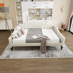 a white bed sitting on top of a wooden floor next to a book shelf filled with books