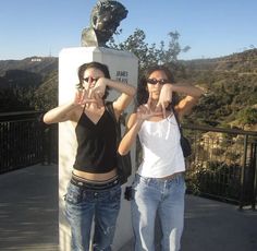 two young women standing next to a statue with their hands in the air and making faces