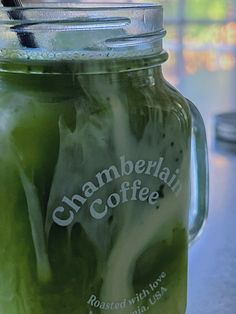 a jar filled with green liquid sitting on top of a table next to a cup