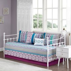 a white daybed with purple and blue pillows in a living room next to a window