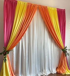 an orange, yellow and pink drapes are hanging on the wall next to a wooden floor