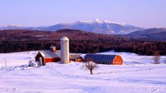 a barn and silo in the snow with mountains in the backgrouds