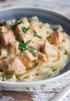 a bowl filled with pasta and meat covered in sauce on top of a wooden table