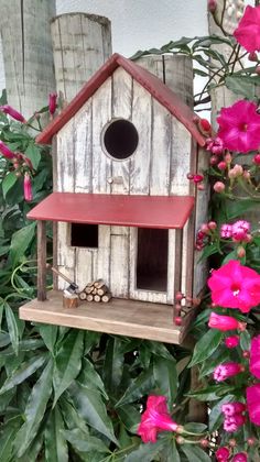 a bird house sitting on top of a wooden table next to pink flowers and greenery