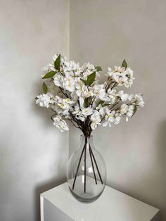 a vase filled with white flowers sitting on top of a table next to a wall