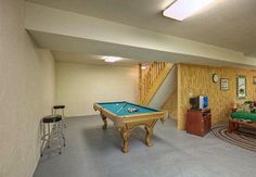 a pool table in the middle of a living room with stairs leading up to it