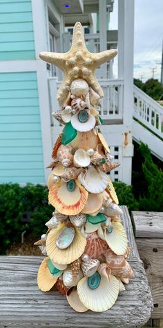 a christmas tree made out of seashells on a wooden bench in front of a house