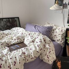 an unmade bed in a bedroom with books on the nightstand and pictures hanging above it