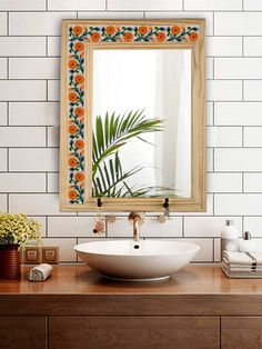 a bathroom sink sitting under a mirror on top of a wooden counter next to a vase with flowers