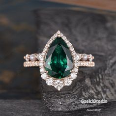 a green and white diamond ring on top of a black stone slab with pearls around it