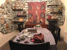 a dining room table covered in clutter next to a stone wall with an art work on it