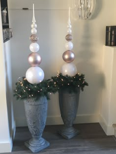 two silver vases with christmas decorations on them sitting in a hallway next to a wall