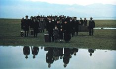 a large group of people standing in front of a body of water with mountains in the background