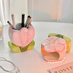 two pink flower shaped containers on top of a white table next to a candle holder